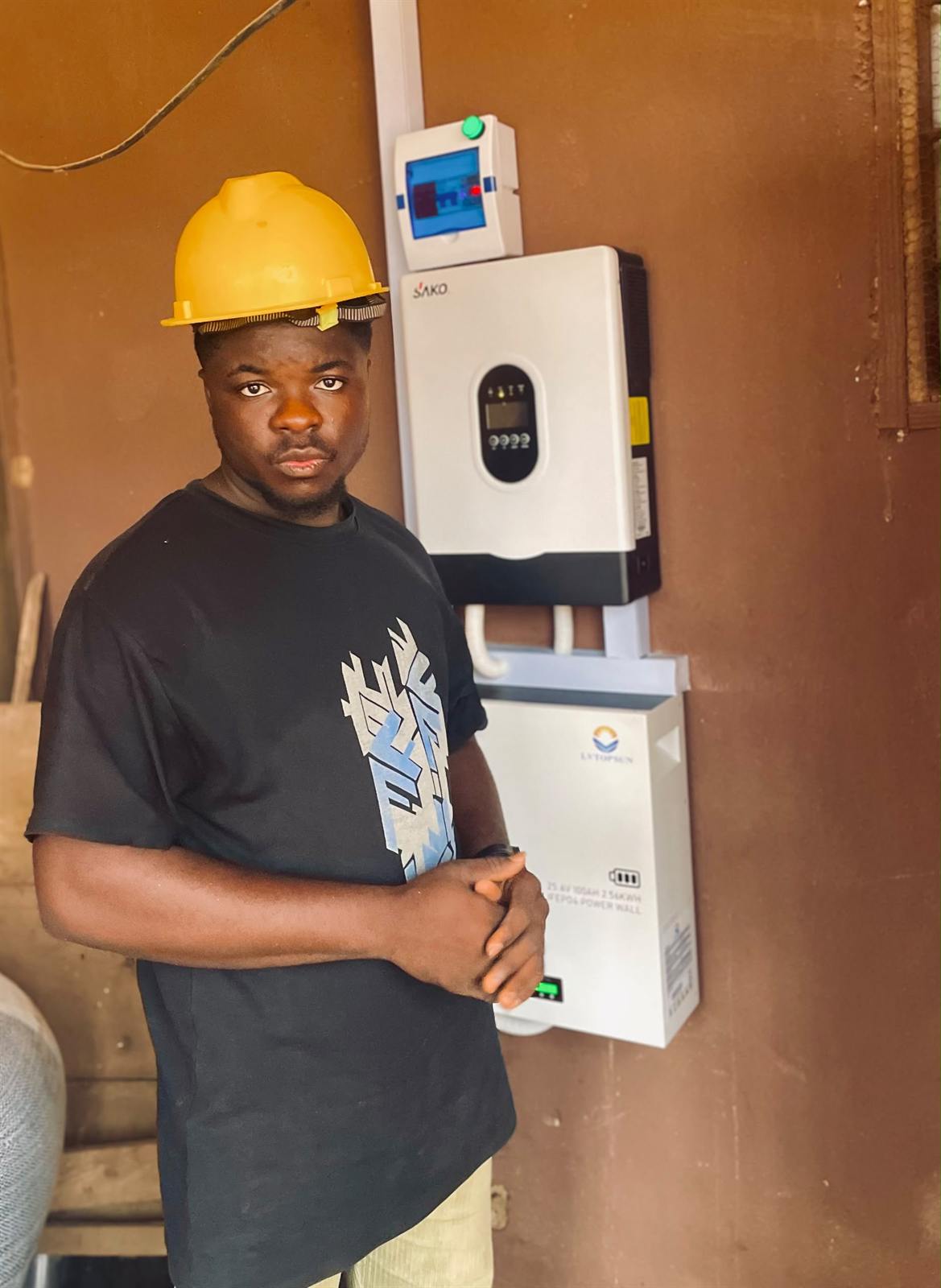 SetGlobalTech installer in a hard hat beside a wall-mounted inverter and battery
