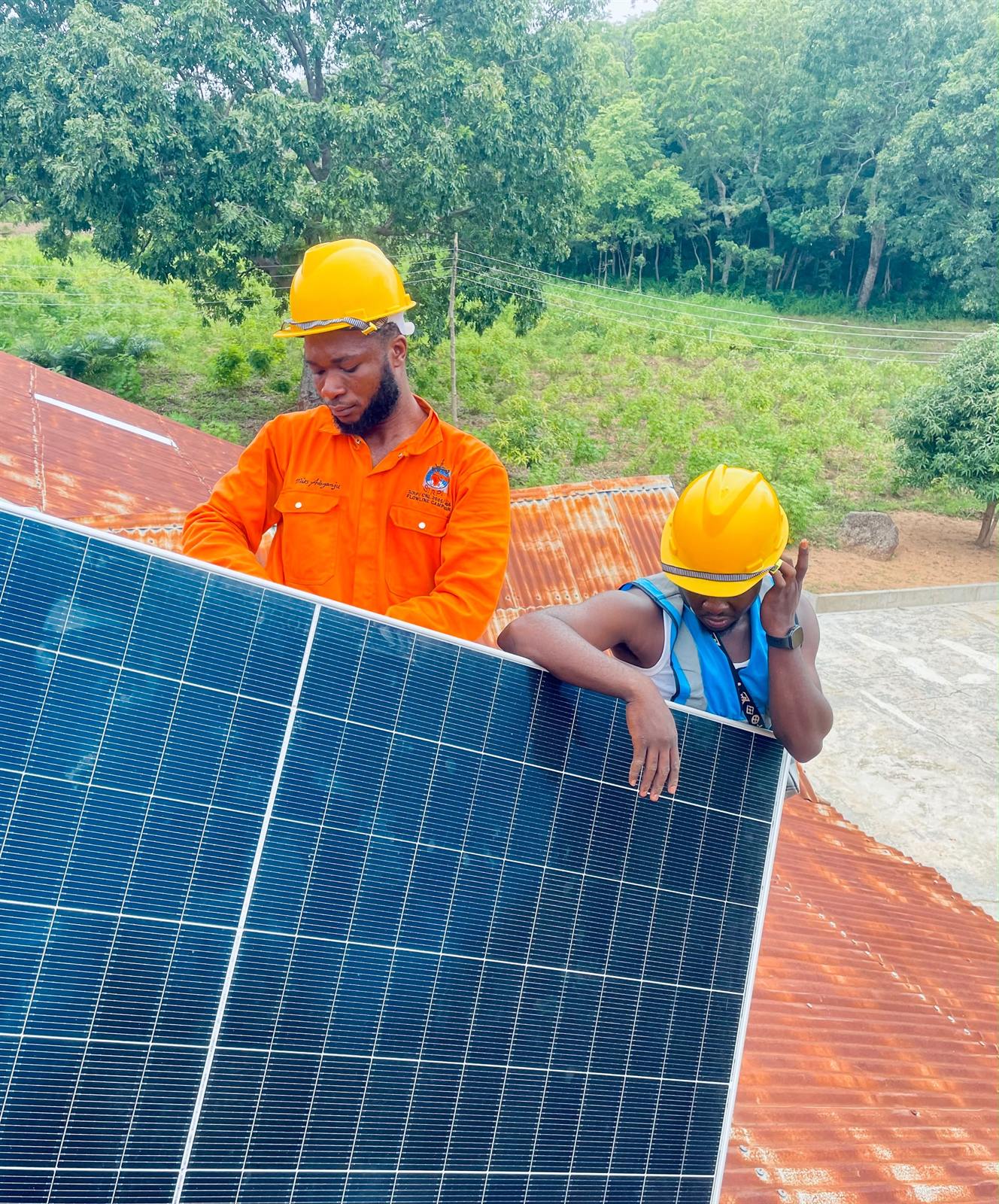 Two installers in hard hats holding a solar panel on a roof